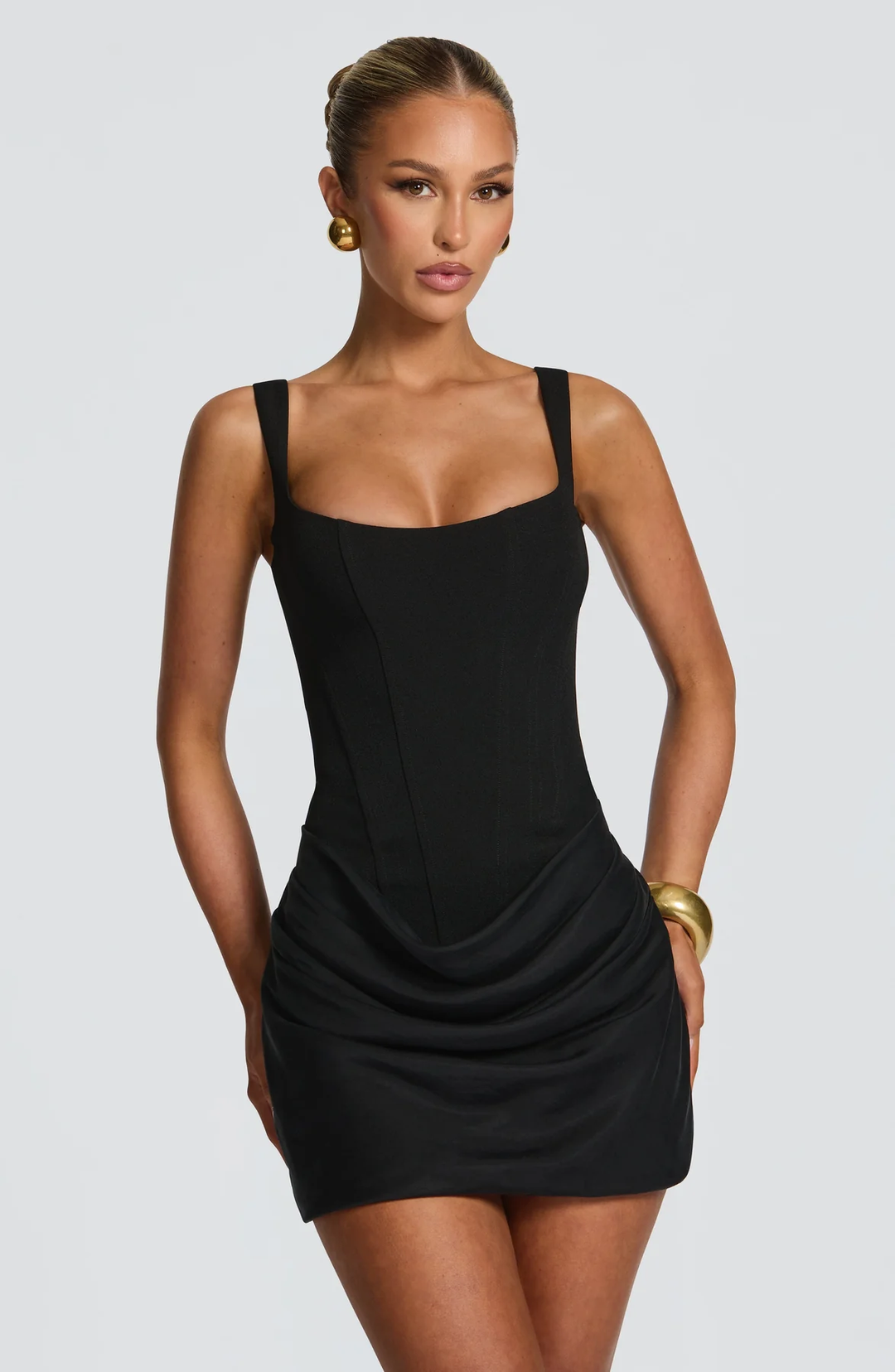 Woman wearing a sleeveless fitted mini dress with soft draping against a plain background.