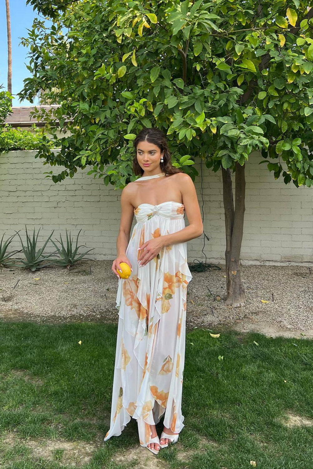 Woman wearing a flowing maxi dress with open back against a plain background.