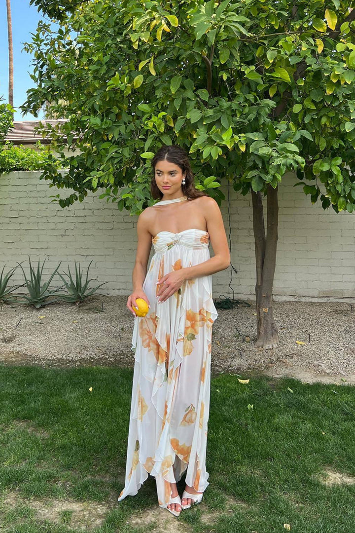 Woman wearing a flowing maxi dress with open back against a plain background.