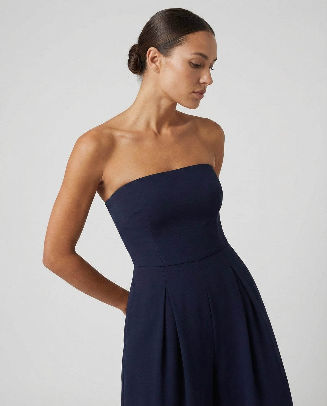 Female model wearing a full-length strapless jumpsuit on a plain background.