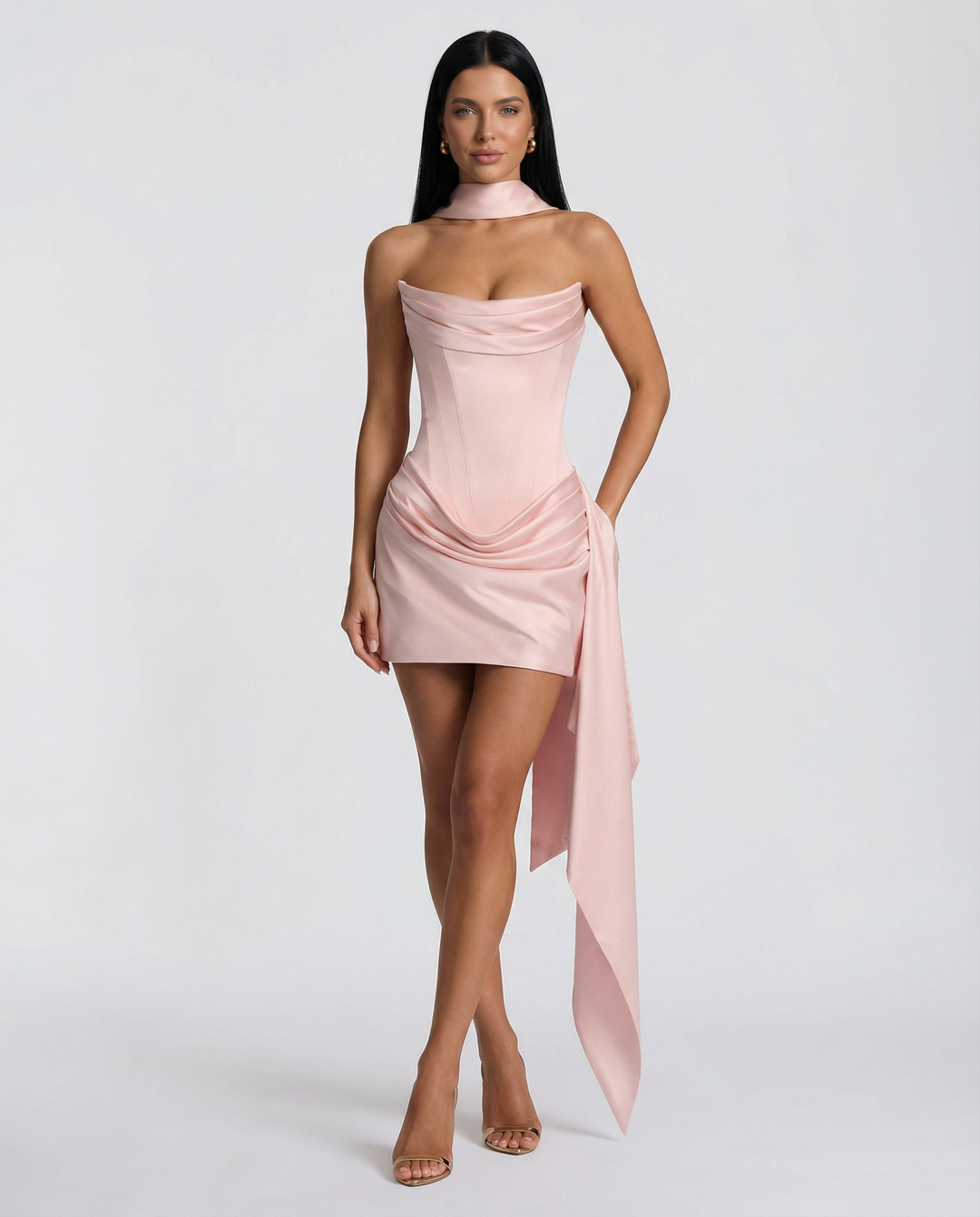Model in a draped strapless mini dress styled for evening wear on a plain background.