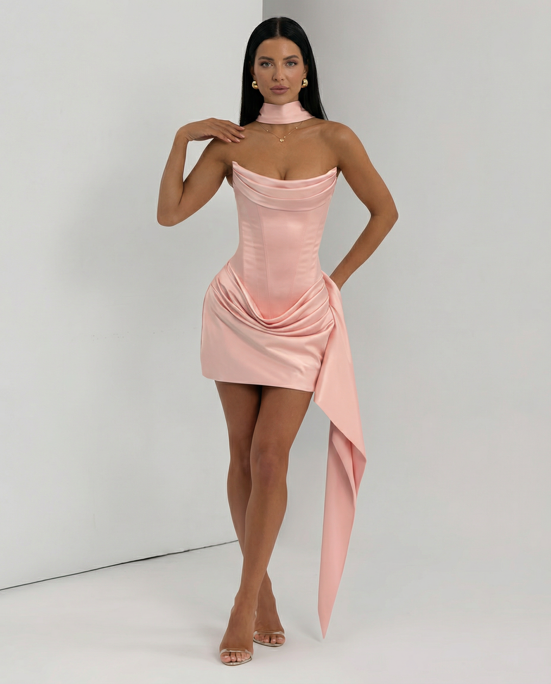 Model wearing a fitted strapless mini dress with modern draped detailing on a plain background.