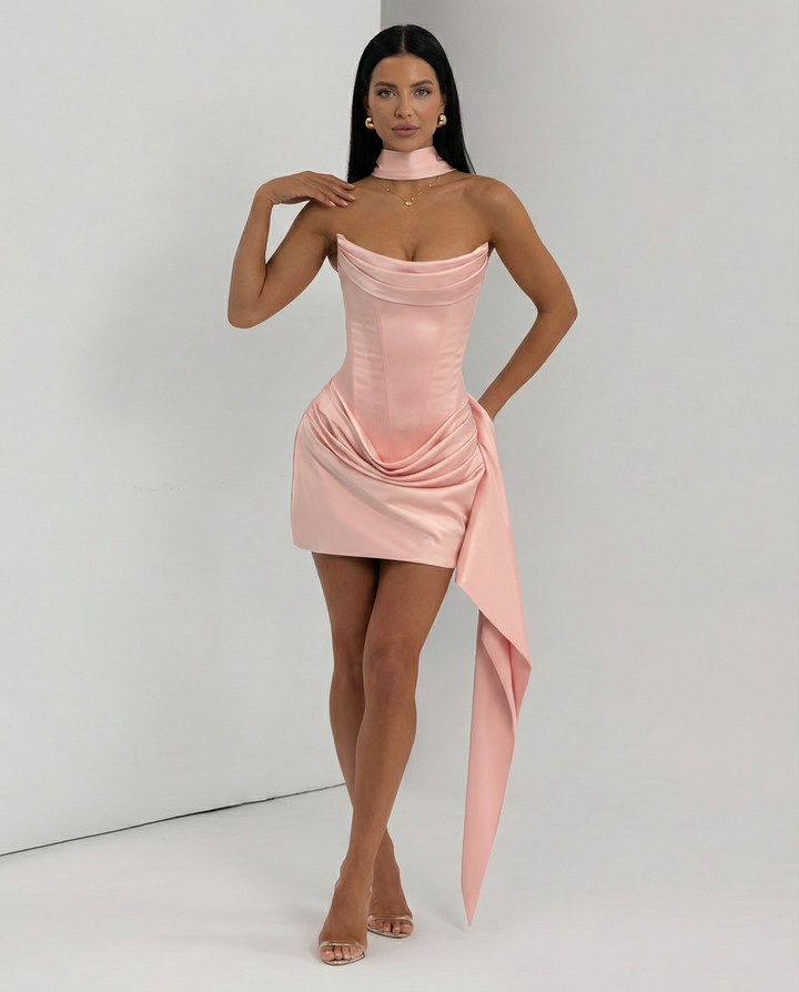 Model wearing a fitted strapless mini dress with modern draped detailing on a plain background.