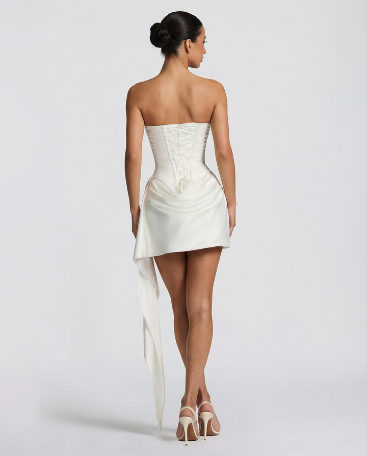 Model wearing a sleeveless strapless mini dress with draped neckline on a plain background.