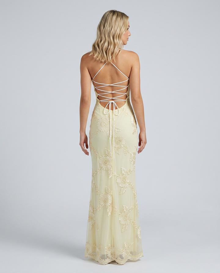 Woman in a fitted maxi dress featuring floral detailing and a lace-up back on a plain background.