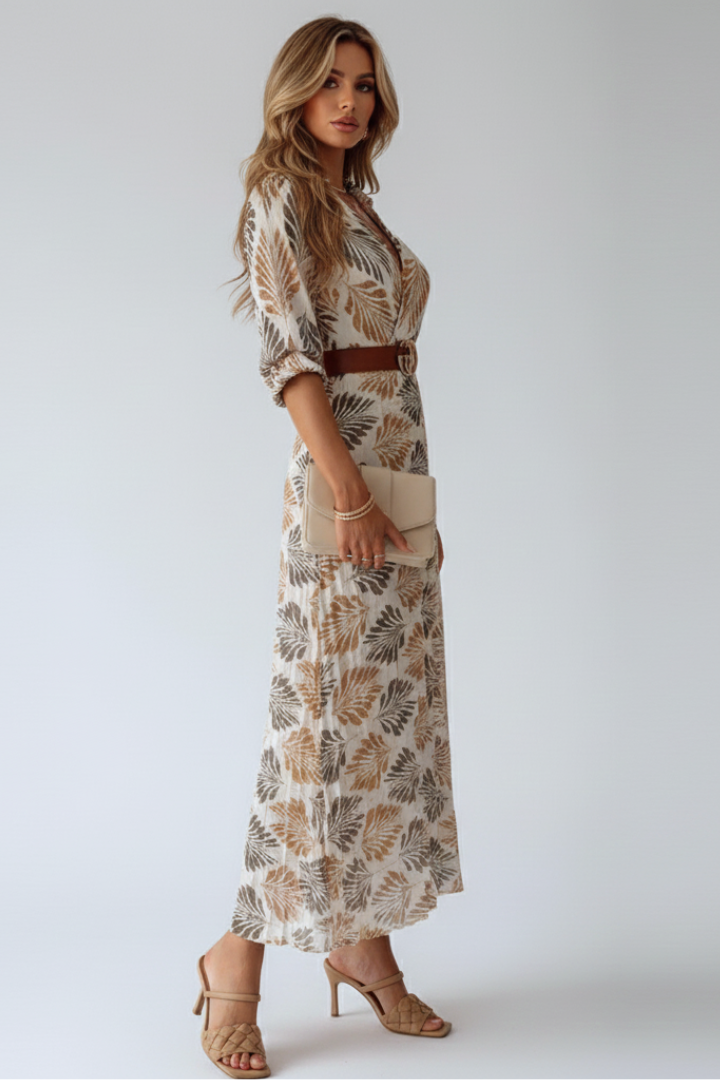 Female model posing in printed long dress on plain gray background.