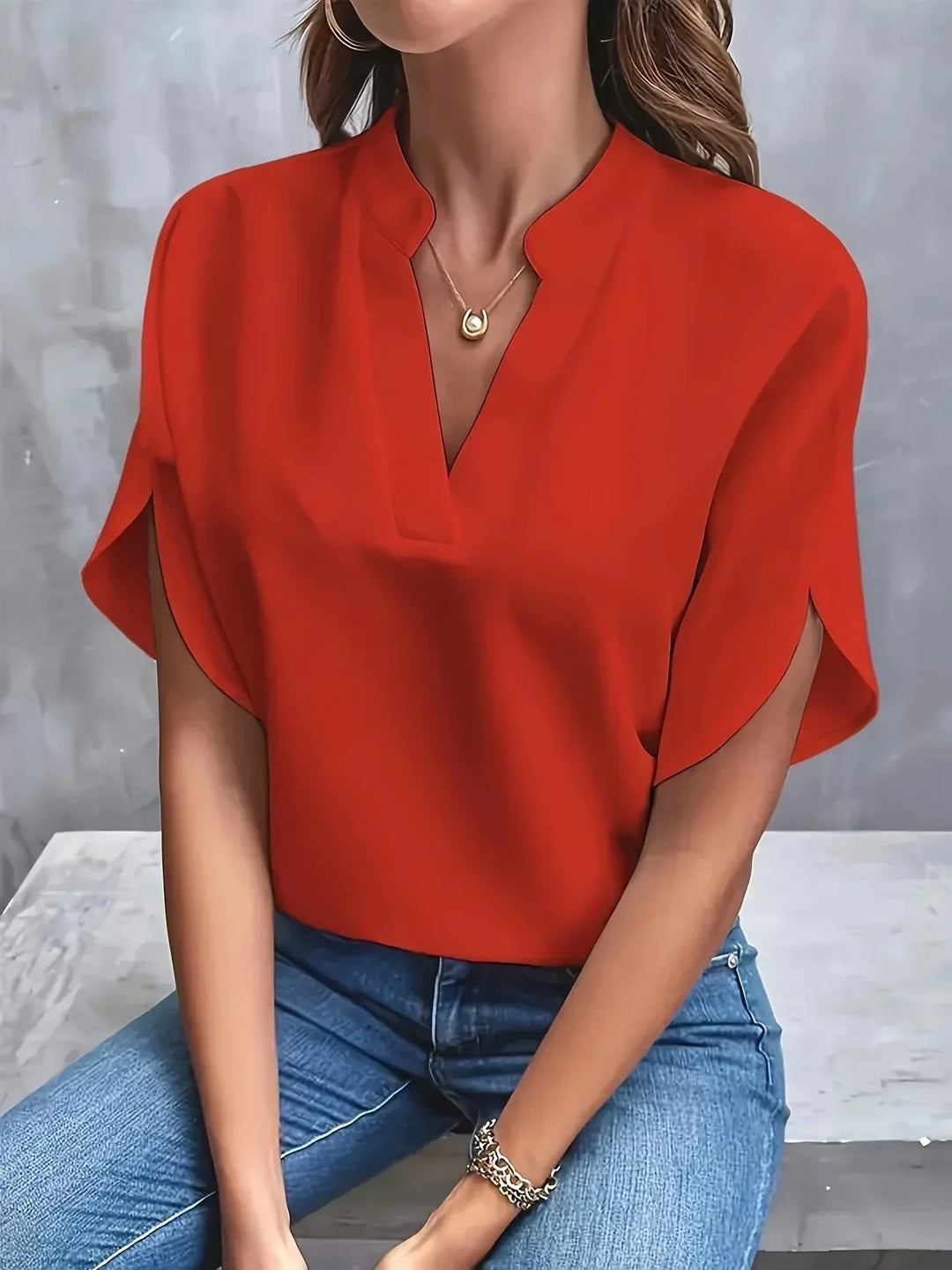 Woman model wearing a minimal summer blouse with flowing sleeves on a plain background.