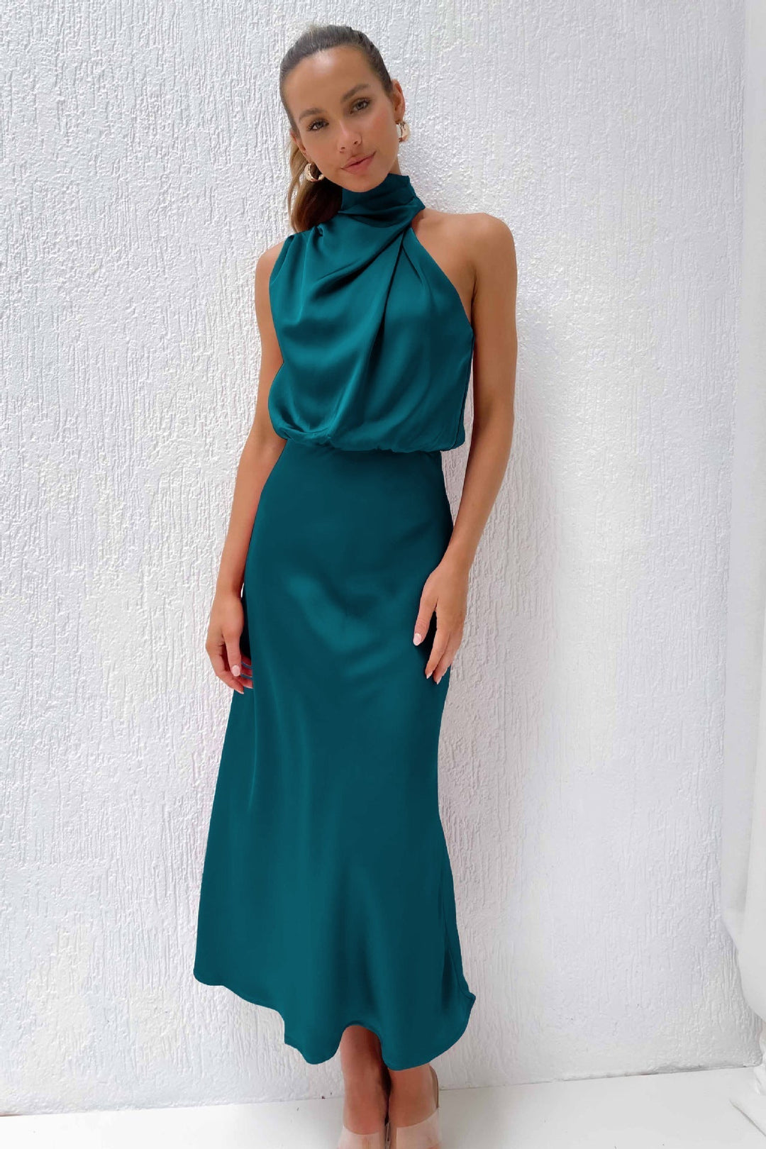  Woman wearing a long draped gown with a timeless appearance against a plain background.