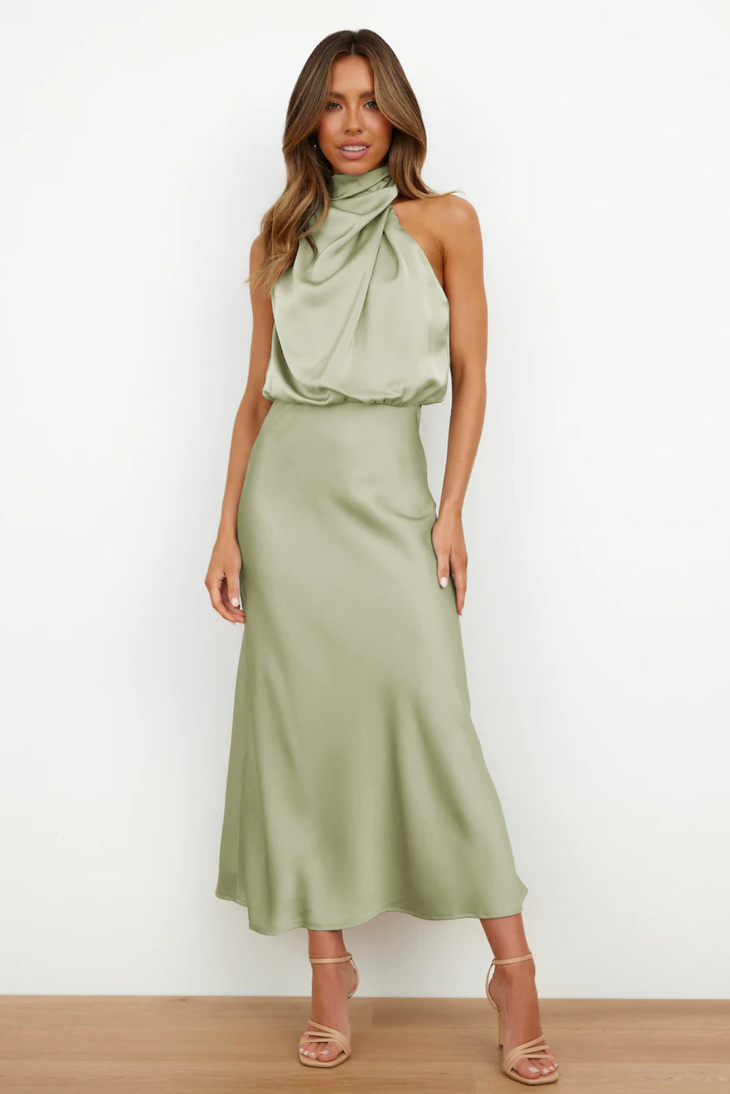 Woman wearing a satin halter evening dress against a plain background.