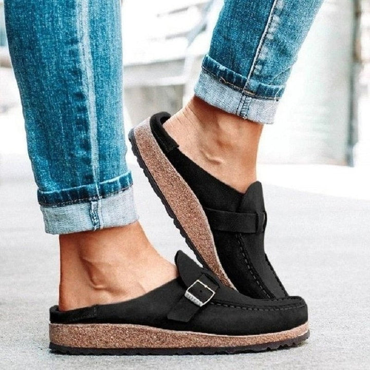 Black sandals with cork sole worn with rolled-up blue jeans on a light background