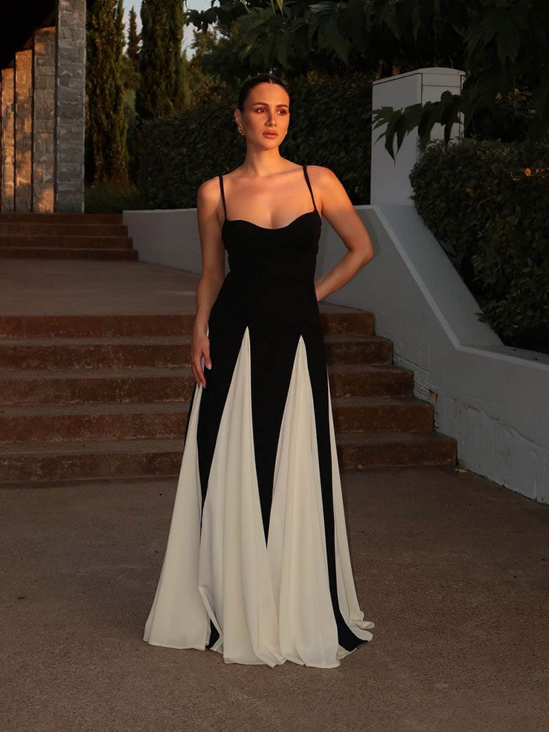 Woman posing in an elegant asymmetrical dress with open-back detail against a staircase background.