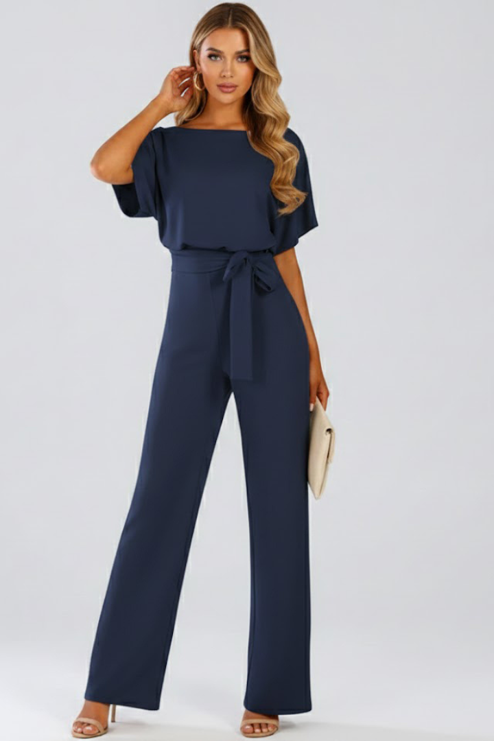 Female model showing a wide leg jumpsuit with round neckline and centered tie detail on a plain background.