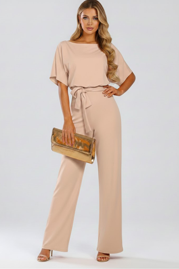 Female model wearing a full-length wide leg jumpsuit with round neckline and waist tie on a plain background.