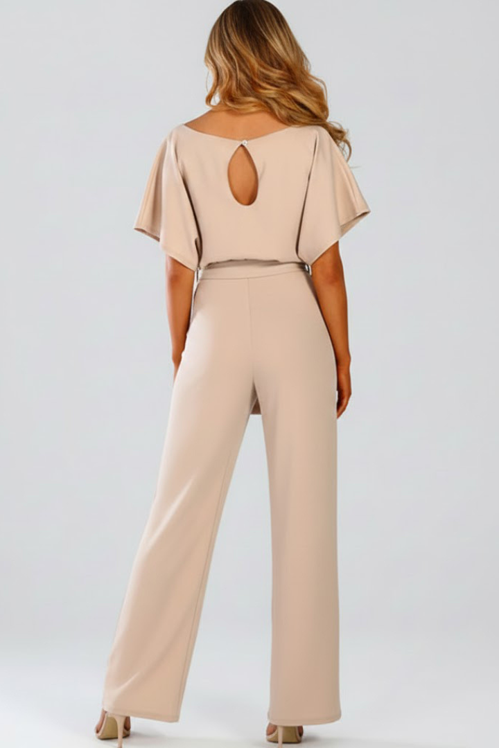 Woman in a short sleeve jumpsuit with tied waist and long wide legs against a plain background.
