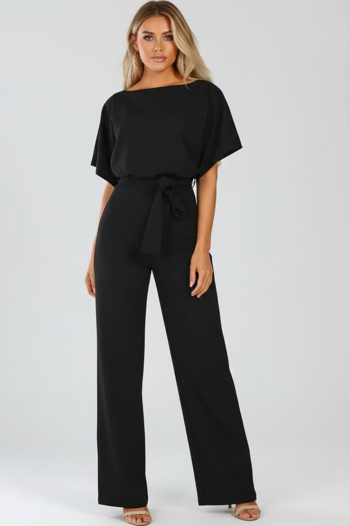 Female model in a one-piece jumpsuit featuring short sleeves and wide leg cut on a plain background.