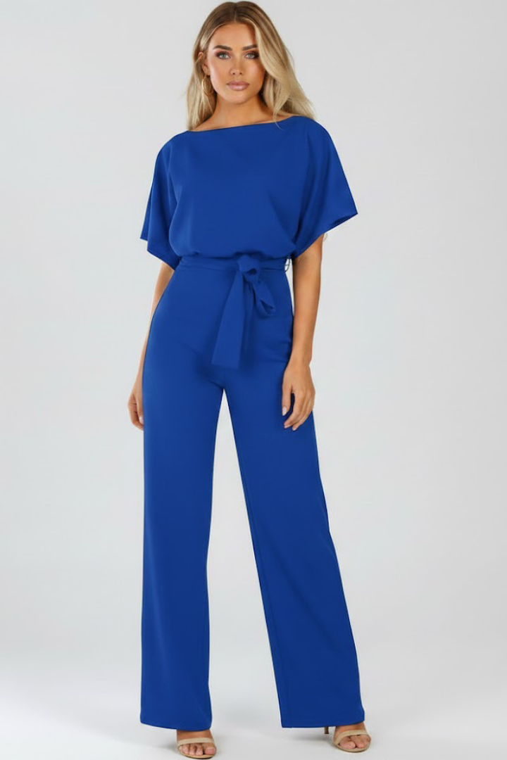 Woman wearing a round neck jumpsuit with a tied waist and full-length legs on a plain background