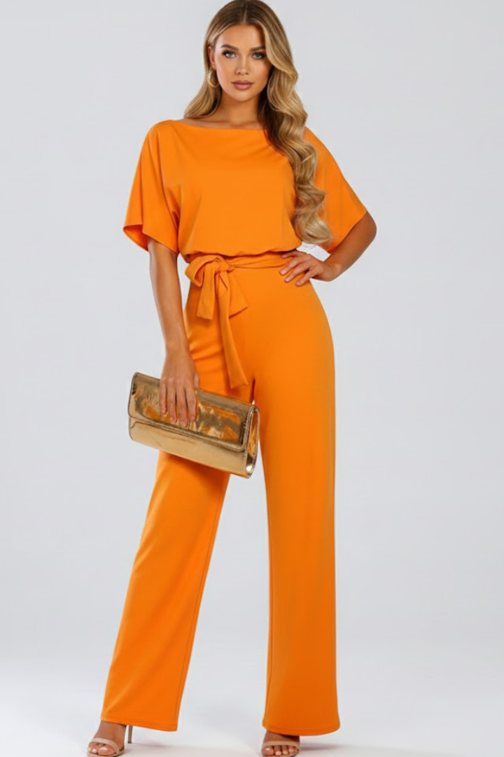 Model dressed in a women’s jumpsuit with waist tie and wide leg outline on a plain background.