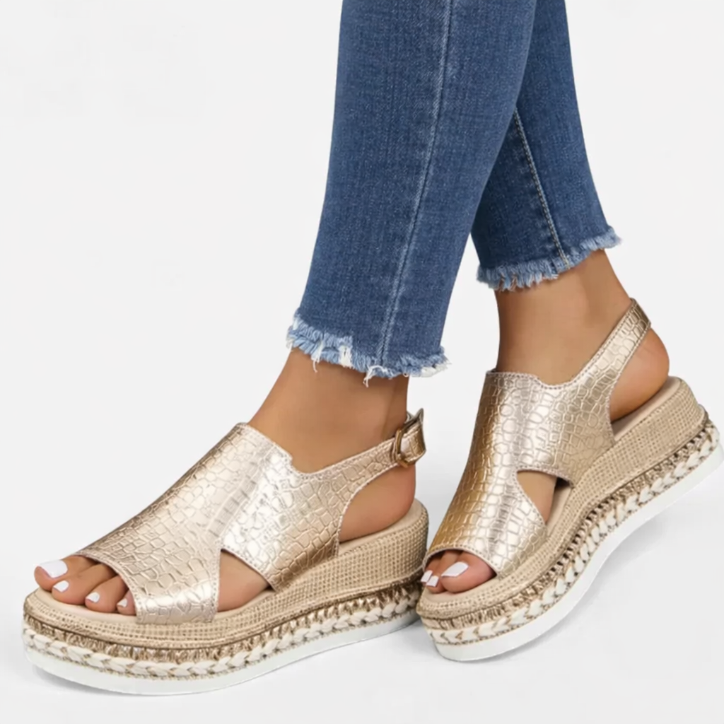 Woman foot wearing metallic platform sandals with buckle straps on a plain background.