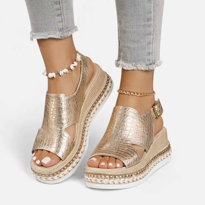 Woman foot styling open-toe wedge sandals with a textured finish on a plain background.