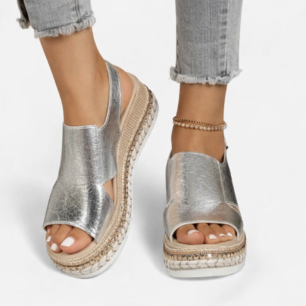 Female foot wearing metallic wedge sandals on a plain background.