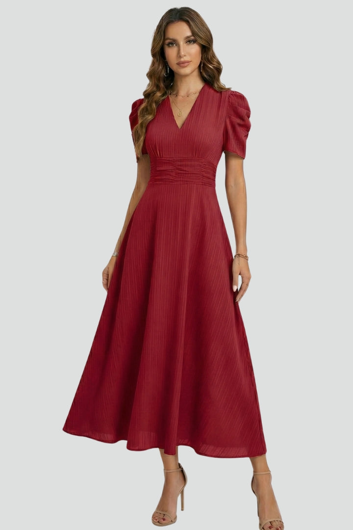 Woman displaying side profile of elegant red dress, plain gray background.