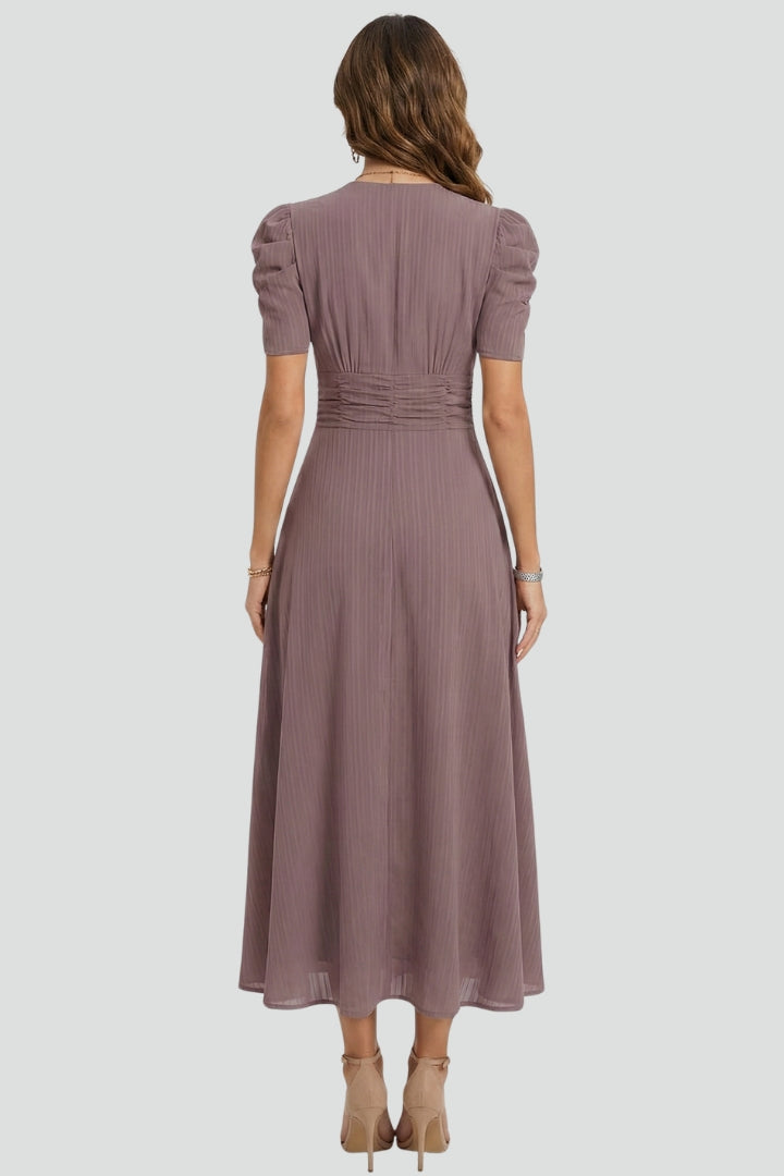 Woman posing in short sleeve dress back angle, plain gray background.