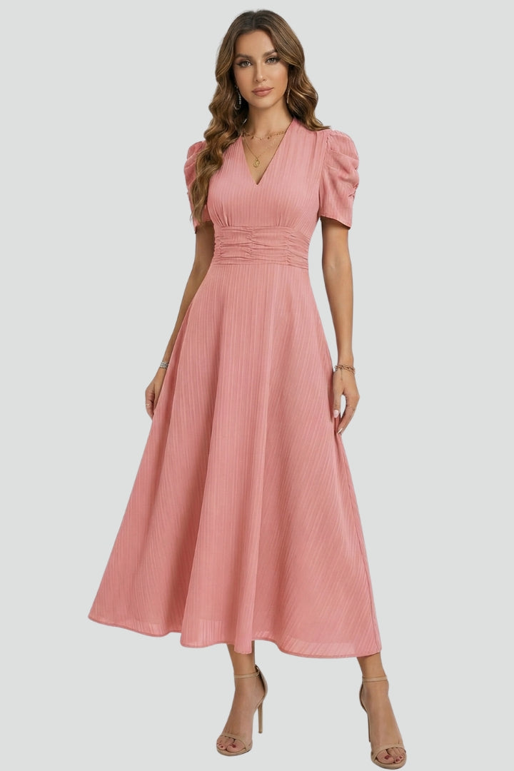 Woman standing in flattering waist dress, plain gray background studio.