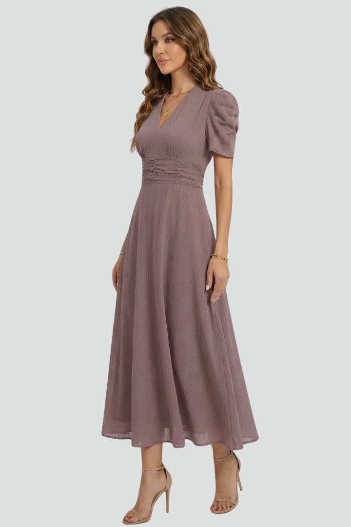 Female model showing ruched waist dress on plain gray background.