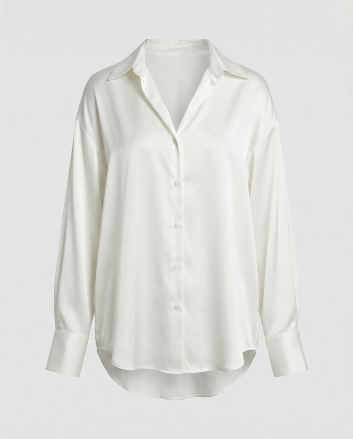 Woman wearing a button-front silk blouse with long sleeves on a plain backdrop.