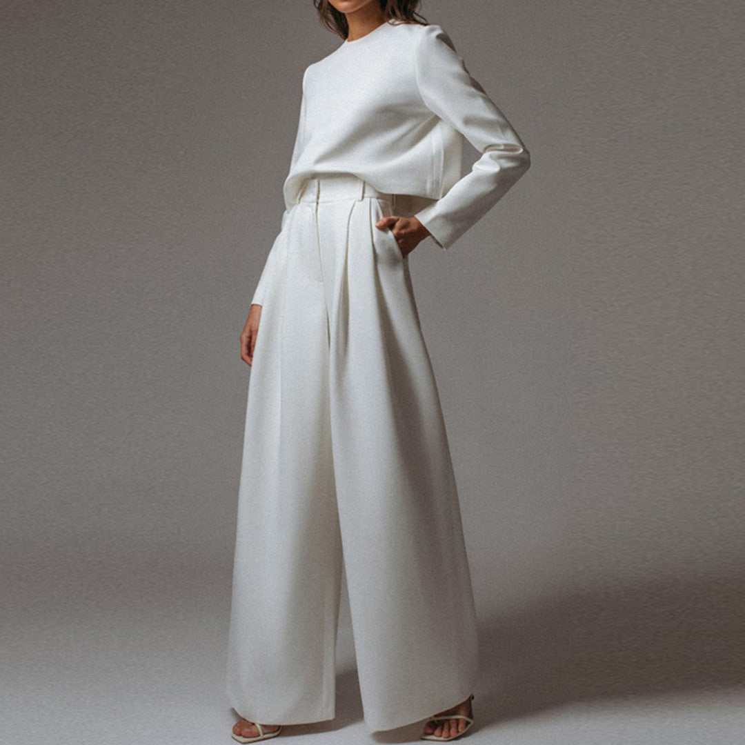 Woman wearing a cropped long-sleeve top and draped wide-leg pants on a plain background.