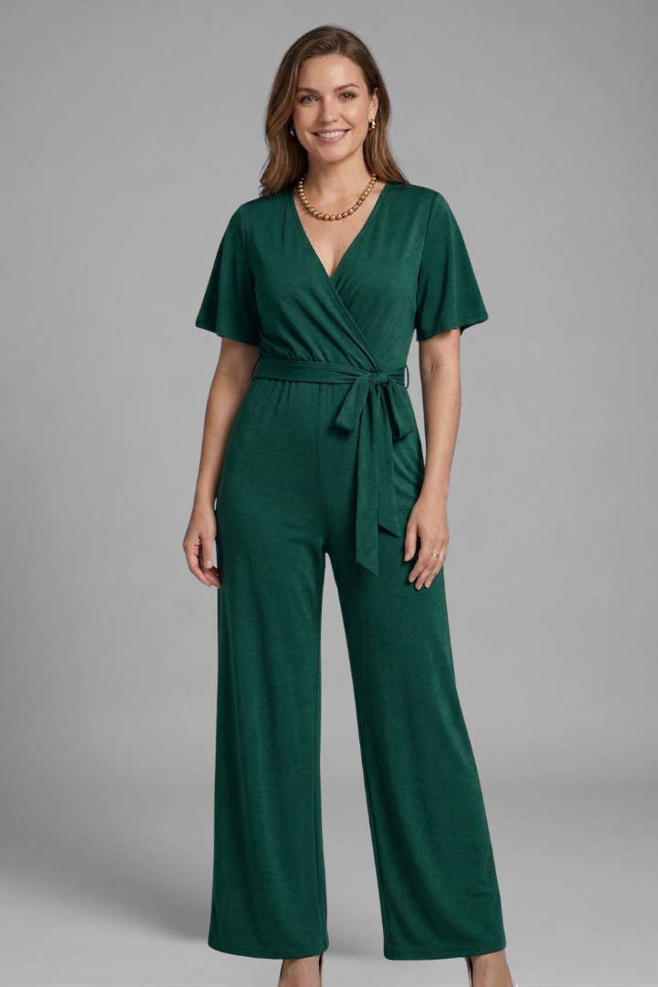 Woman wearing a relaxed fit jumpsuit with short sleeves and tie waist on a plain background.
