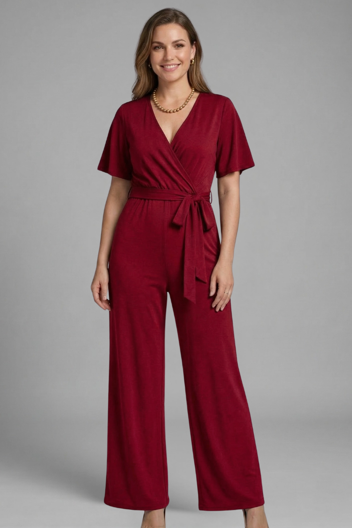 Model wearing a wide leg wrap front jumpsuit with waist tie on a plain background.