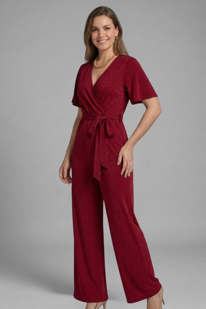 Woman posing in a short sleeve V-neck jumpsuit with adjustable waist tie against a plain background.