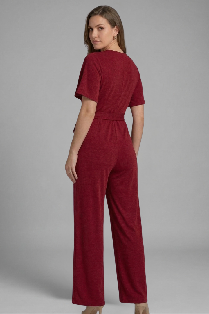 Female model in a full-length wide leg jumpsuit with wrap front detail on a plain background.