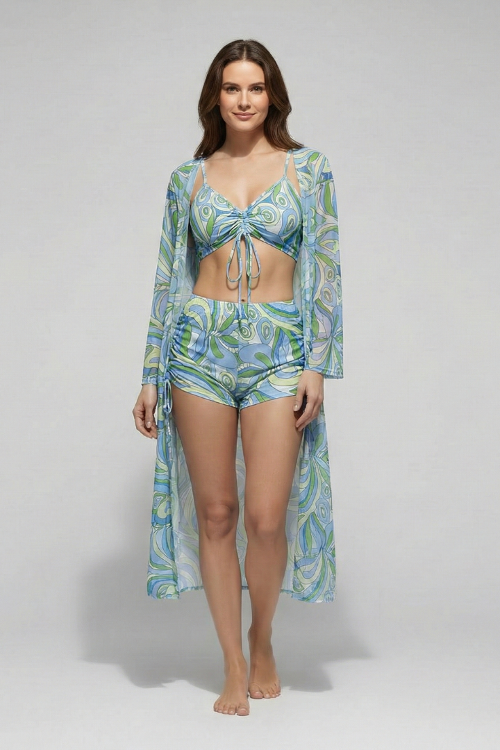 Woman showcasing a matching three-piece swim set with a printed design and lightweight cover-up on a plain background.