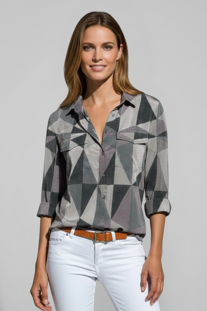 Woman in grey collared top with geometric print design and white pants with belt