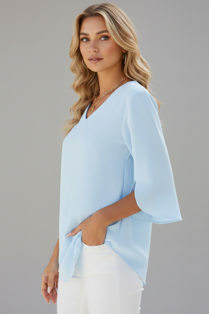 Model wearing fit blouse with V-neckline side view with hand on white pants pocket