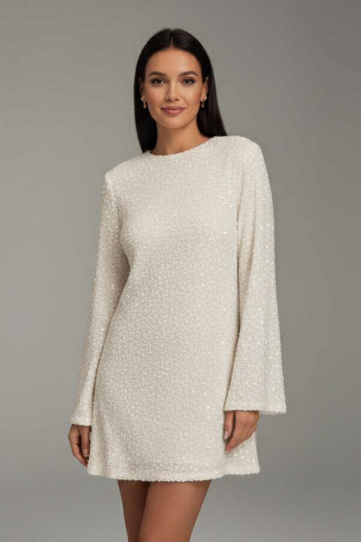 Woman wearing sparkling long sleeve mini dress on plain gray background.
