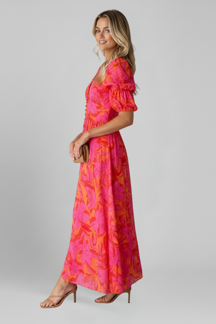 Female model posing in flowing printed dress on plain gray background.