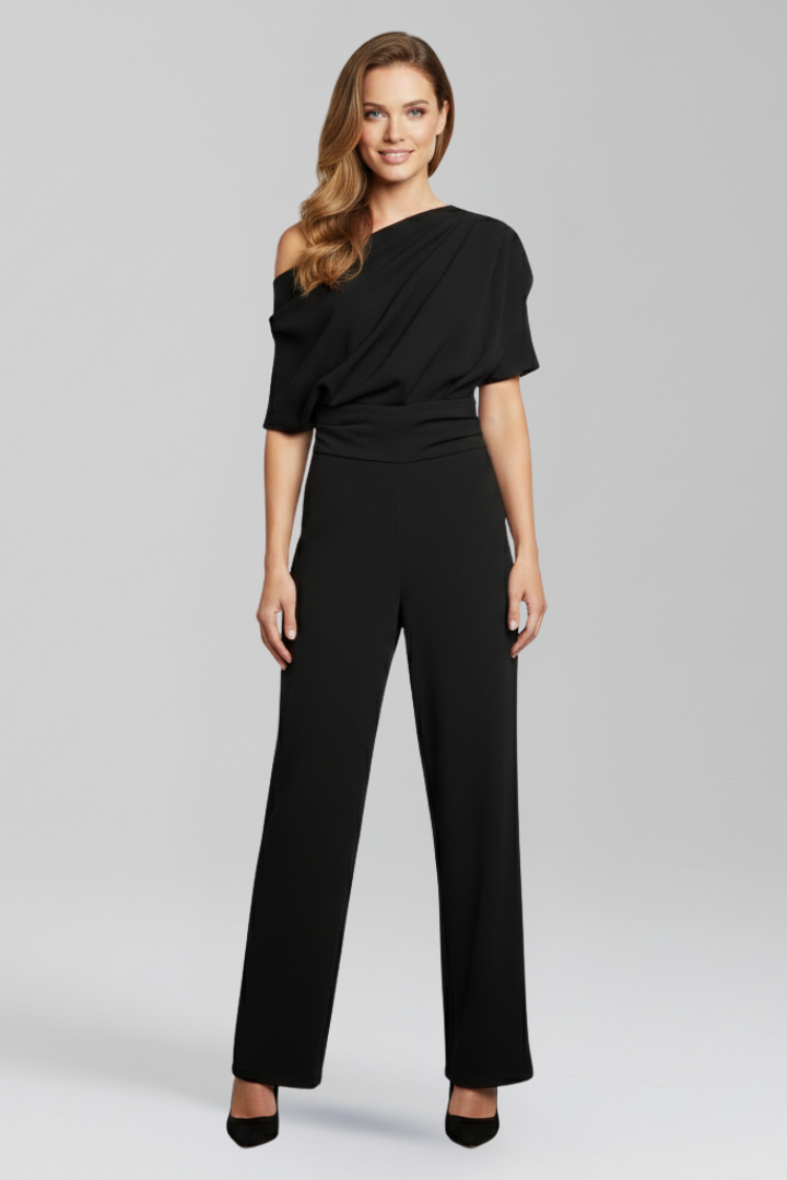 Female wearing a full-length jumpsuit with an asymmetric neckline on a plain background.