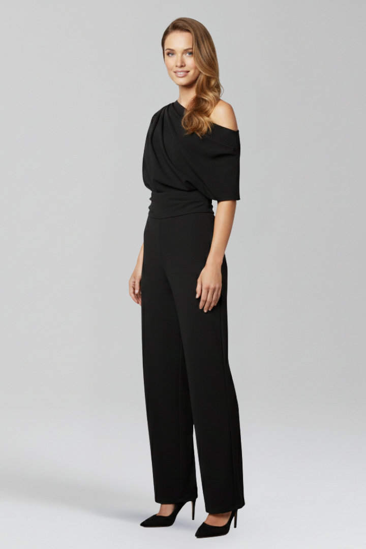 Female in an asymmetric neckline jumpsuit with long sleeves on a plain background.