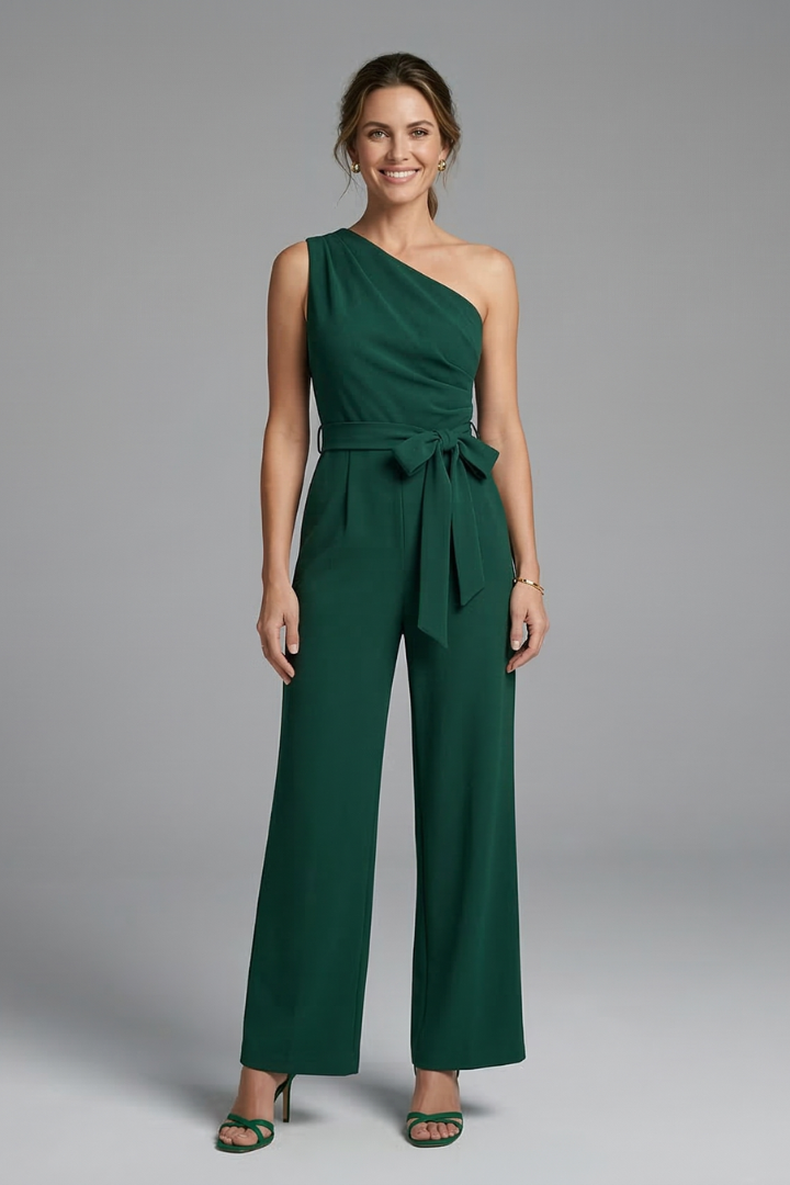 Female model wearing an asymmetric neckline sleeveless jumpsuit with waist belt on a plain background.