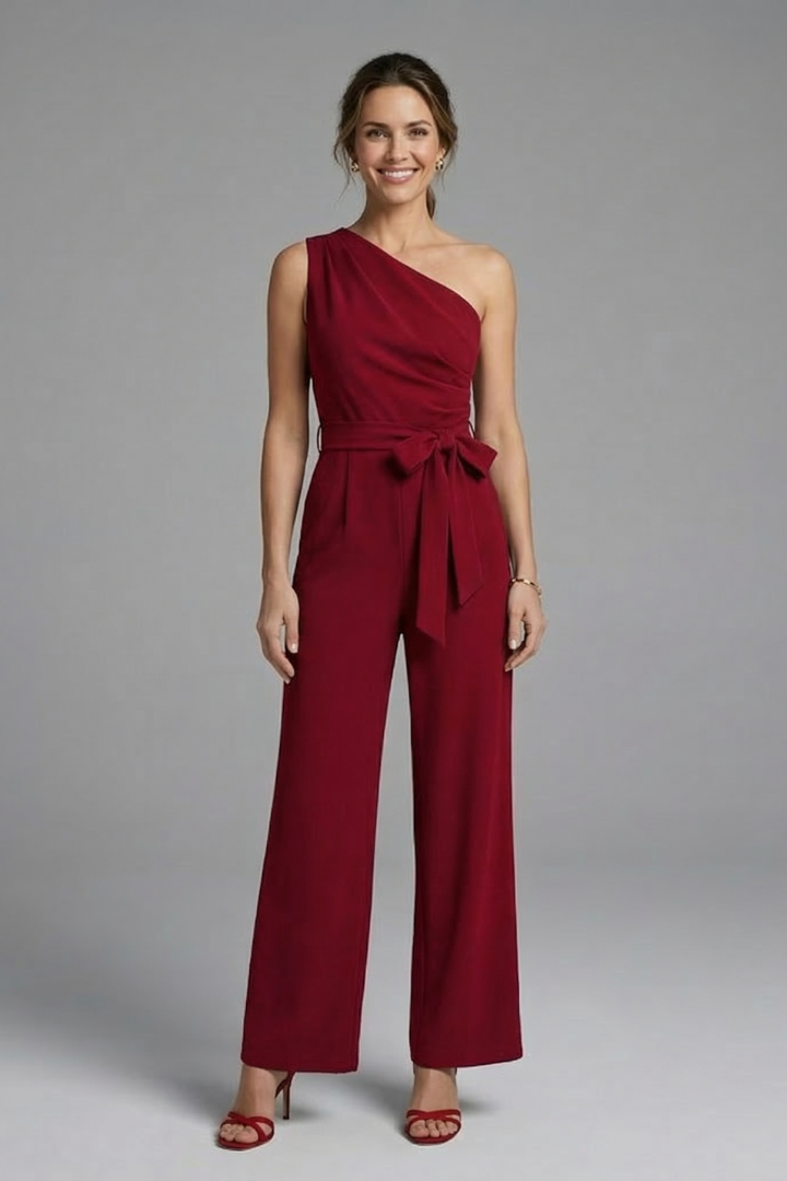 Woman wearing a sleeveless asymmetric jumpsuit with straight wide leg drape on a plain background.