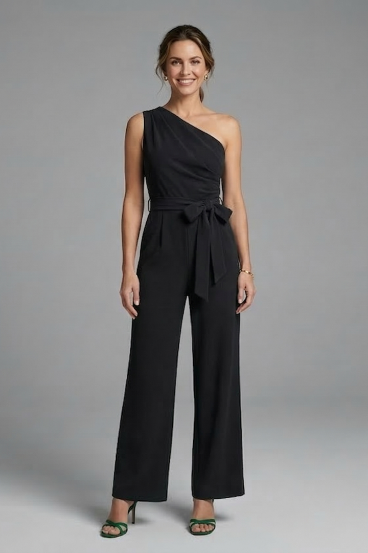Model in a belted waist jumpsuit with asymmetric neckline and full-length legs on a plain background.