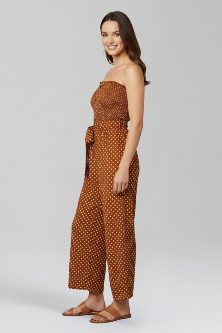 Female model in a bandeau jumpsuit with tie waist and side pockets on a plain background.