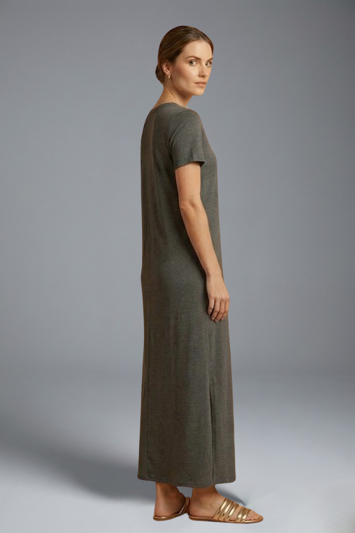 Woman in simple long dress sideway standing gray background