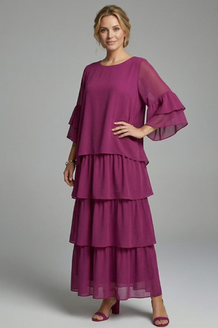 Model wearing an ankle length tiered maxi dress with a rounded neckline on a plain background.