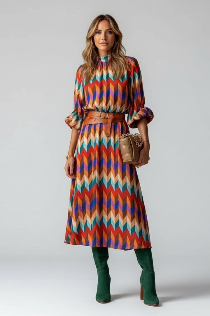 Female model wearing colourful geometric midi dress on plain gray background.