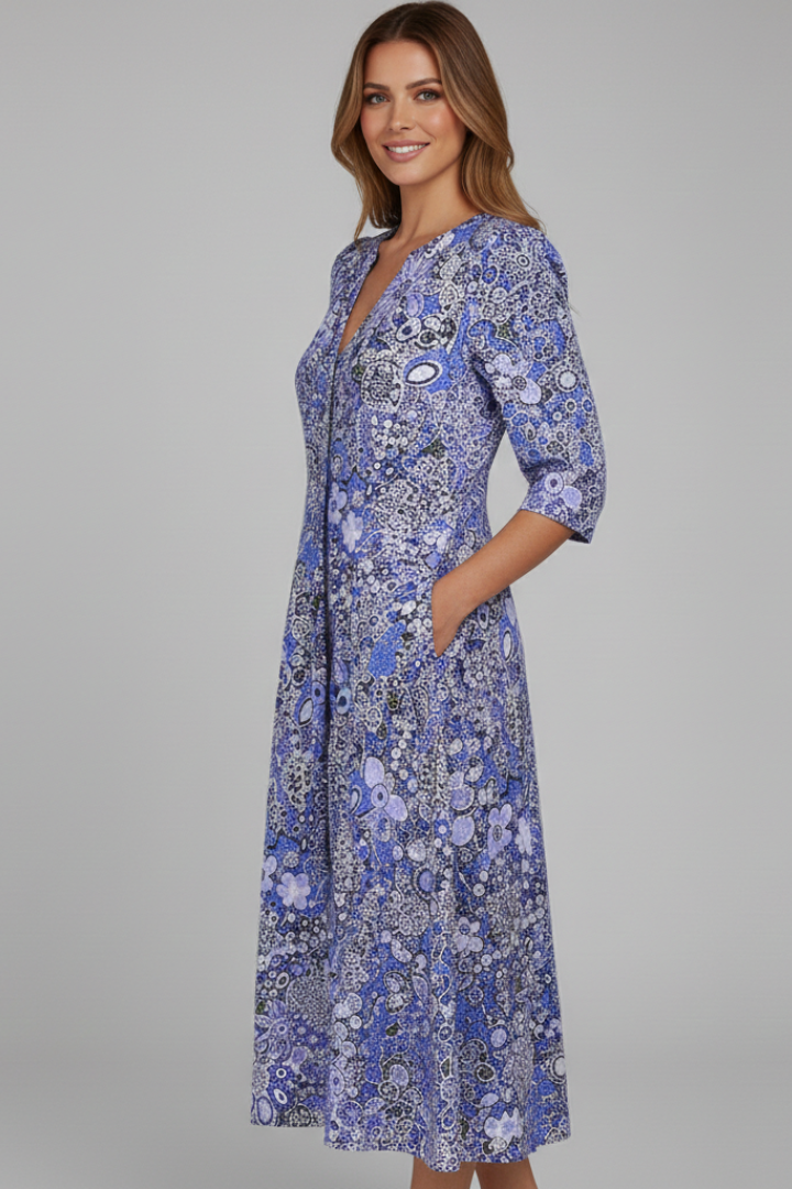 Female model showing V-neck printed dress in front on gray.