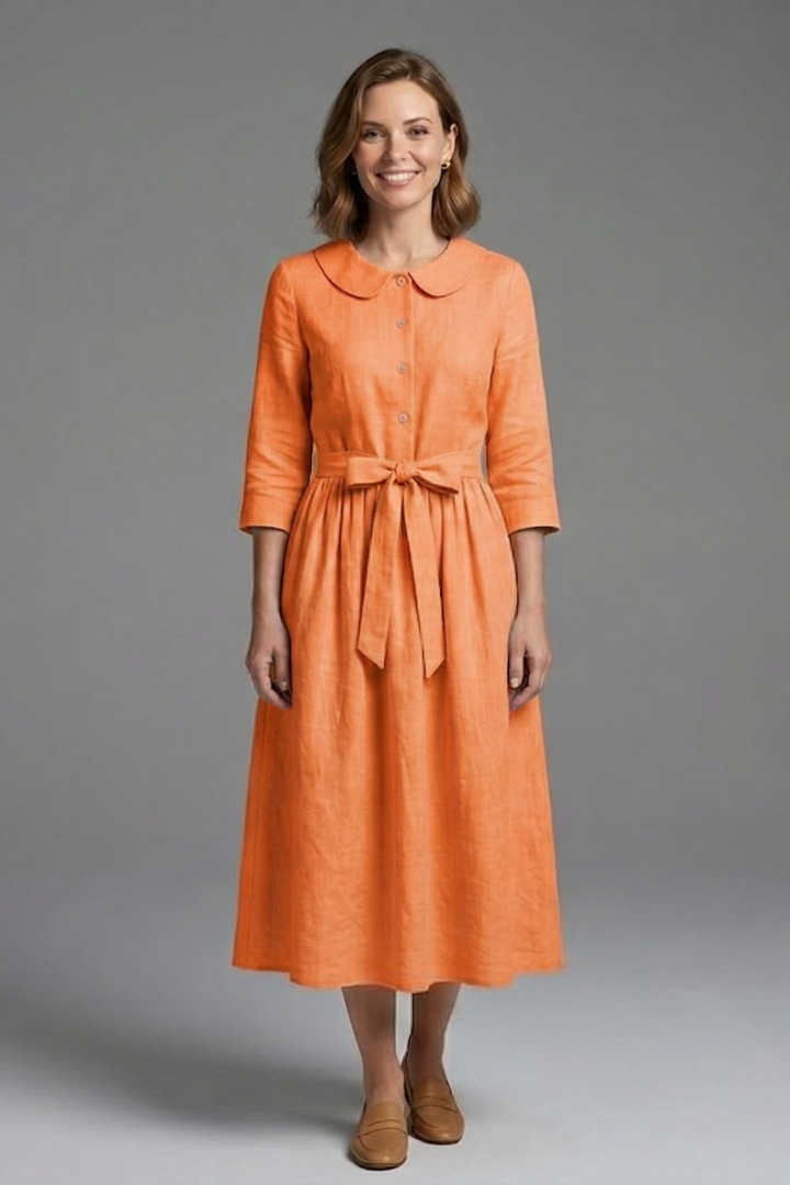 Female model standing naturally in draped dress on gray background.